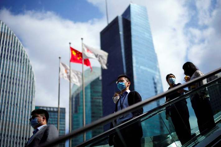 People wearing face masks ride an escalator past office towers in the Lujiazui financial district of Shanghai, China