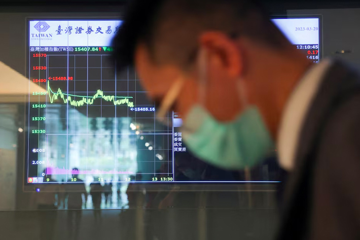 A man wearing a face mask passes in front of screens showing trading data while using an escalator outside Taiwan Stock Exchange in Taipei, Taiwan